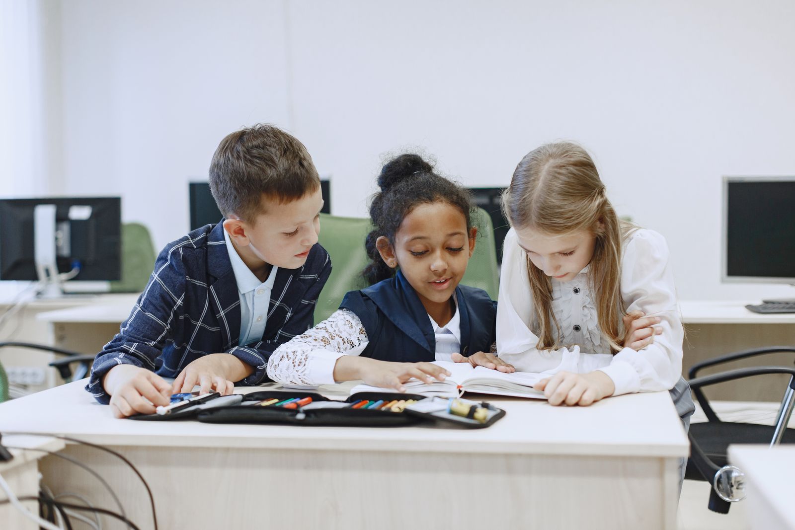 Children working together on a book at a classroom desk.