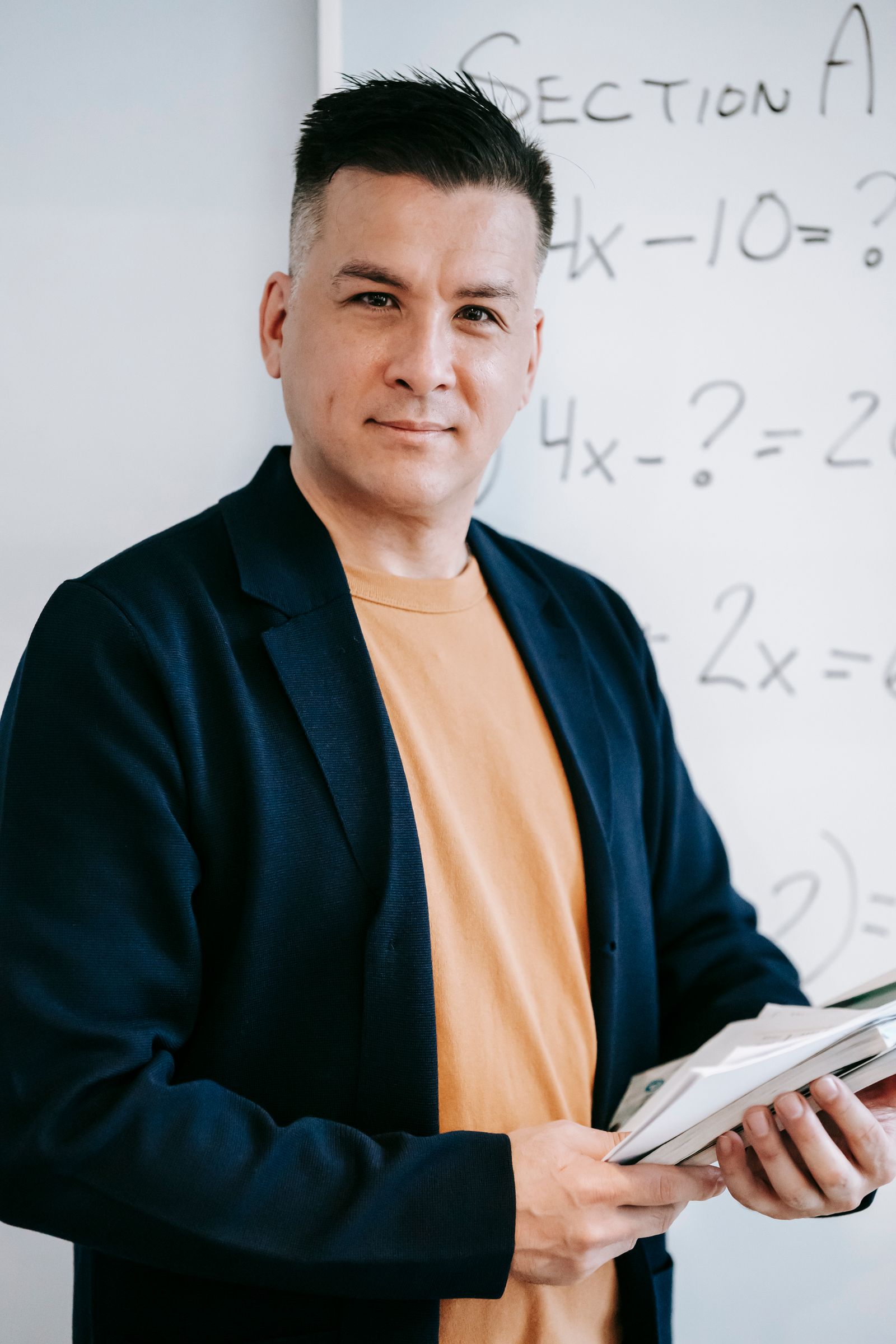 Portrait of a teacher standing in front of a classroom whiteboard.