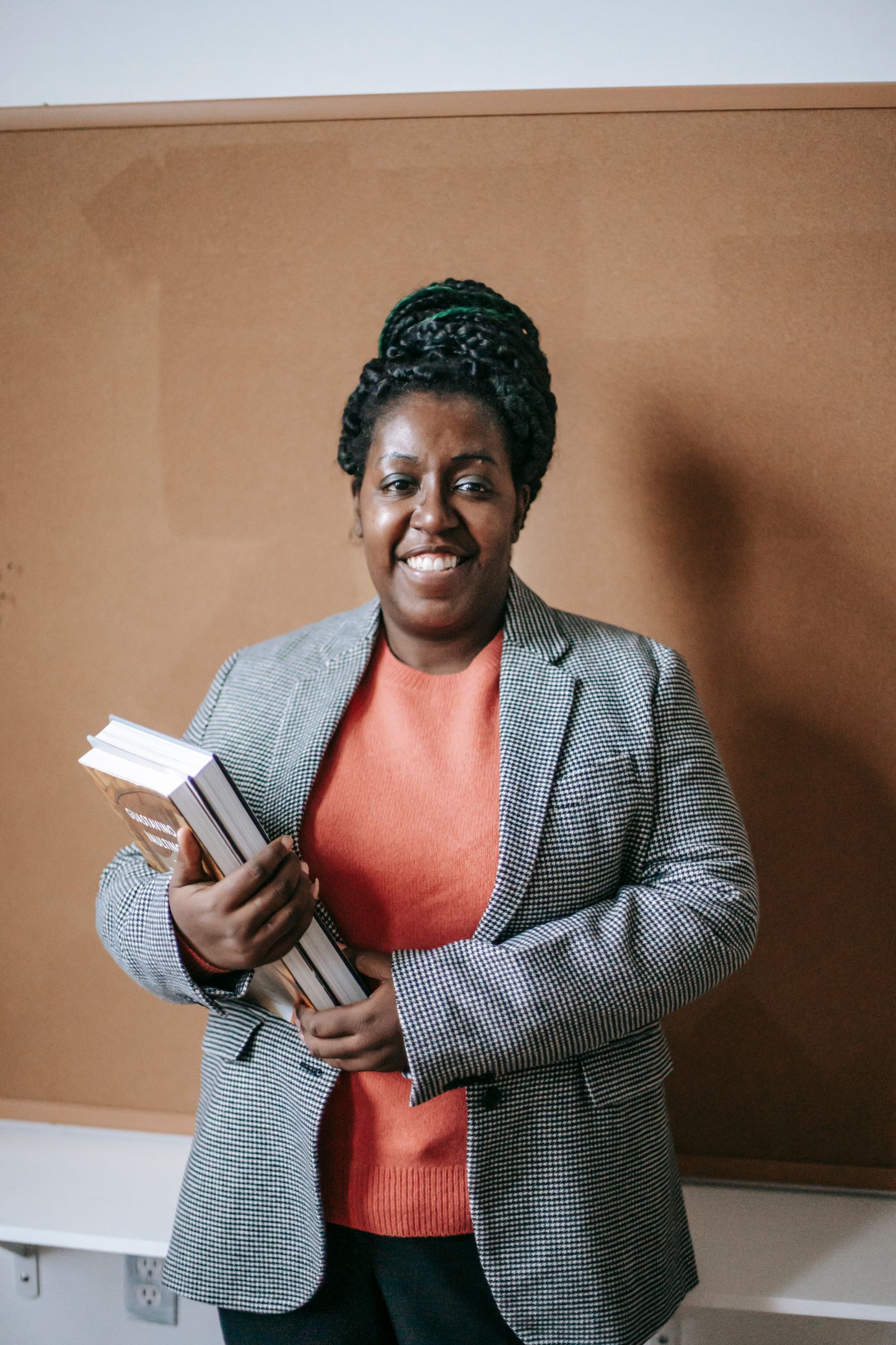 Portrait of a teacher holding books beside a classroom board.