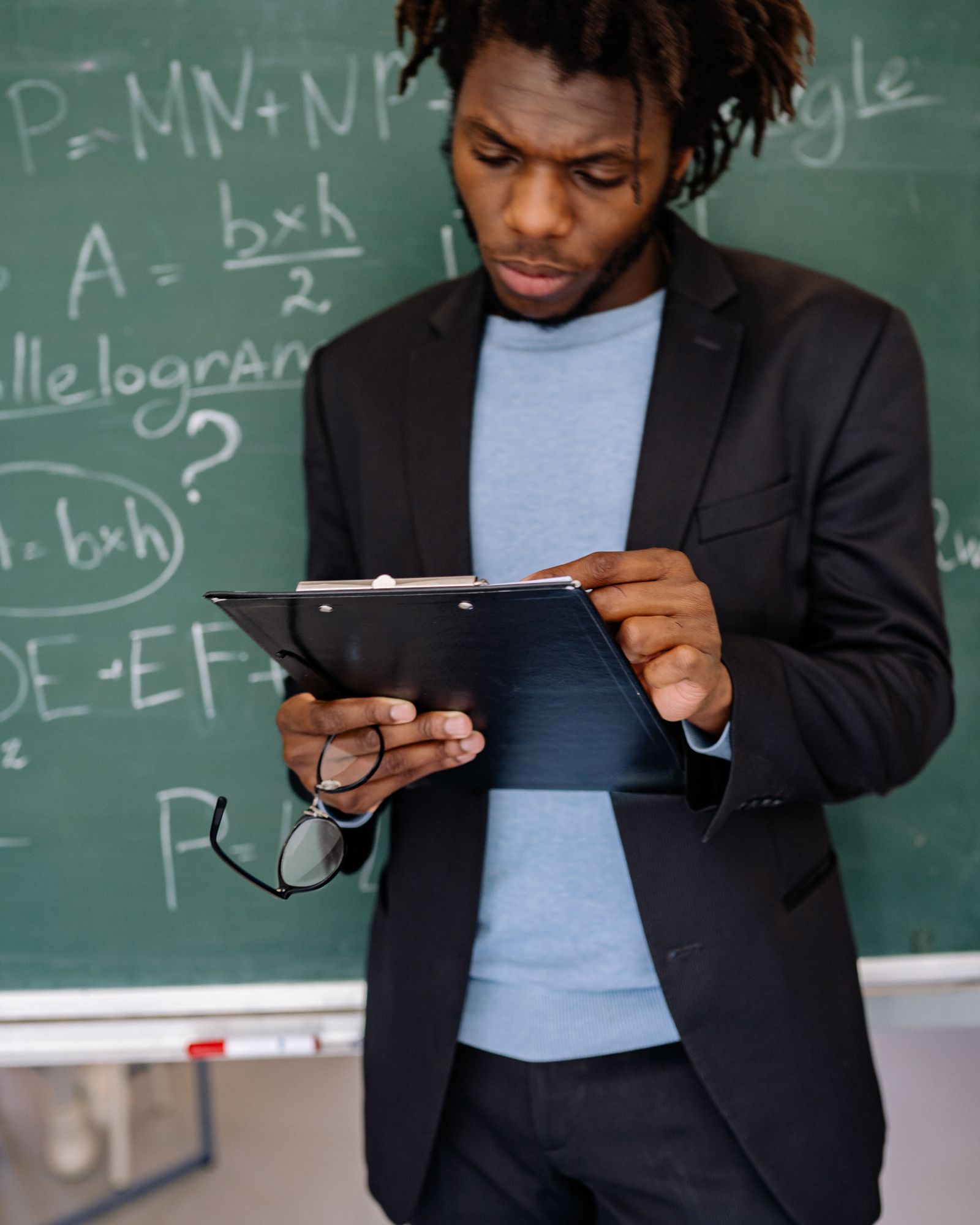 Portrait of a teacher in a blazer reviewing notes beside a blackboard.